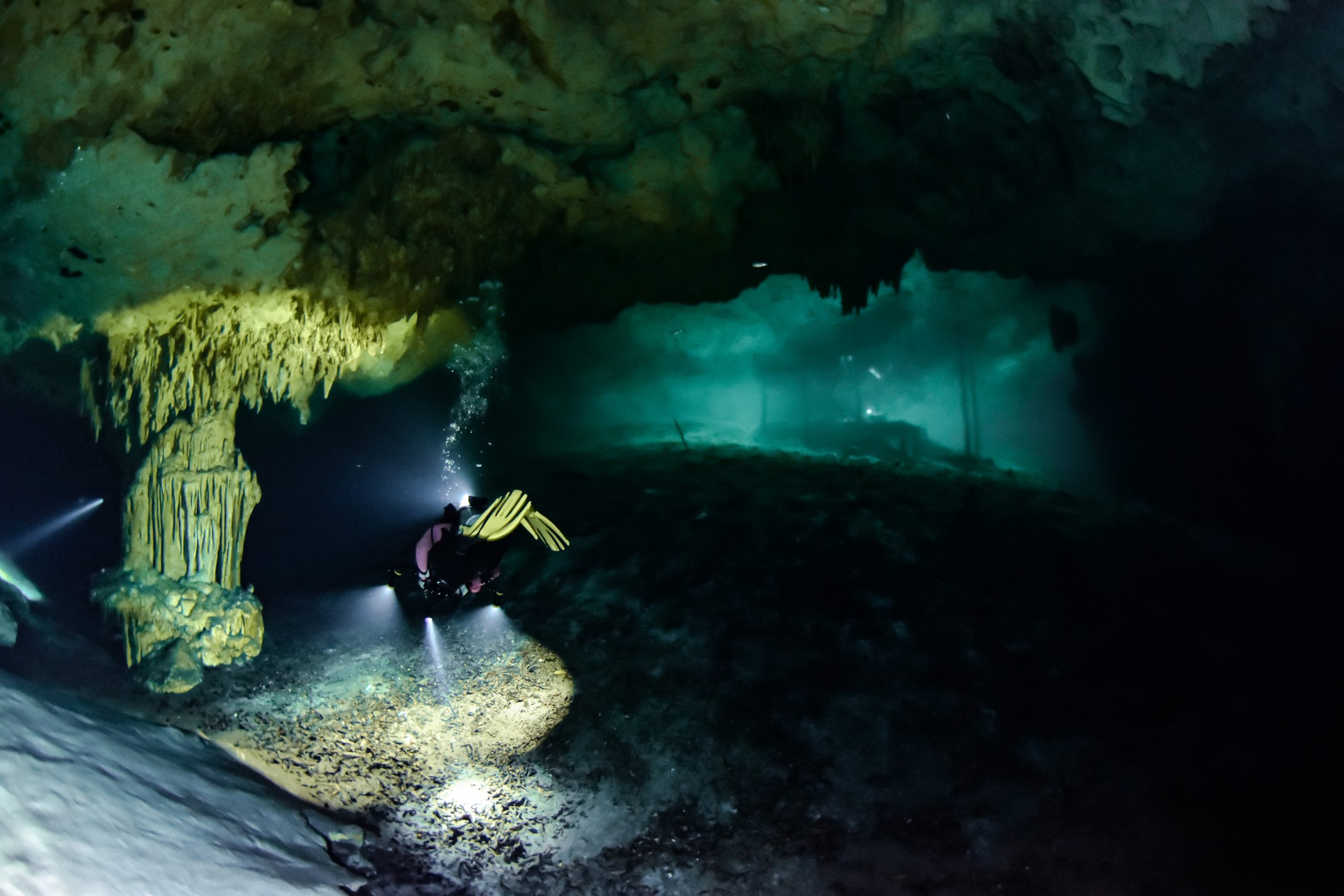 Diver with dive light exploring an underwater cave in a Tulum cenote