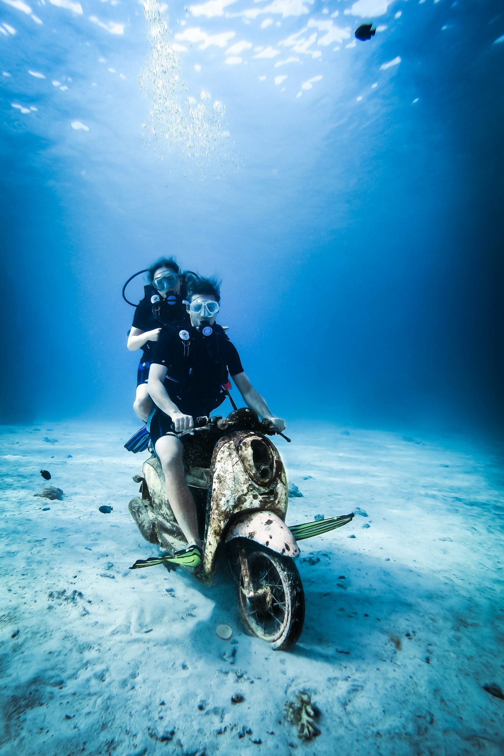 Divers posing on a sunken motorbike underwater in Thailand