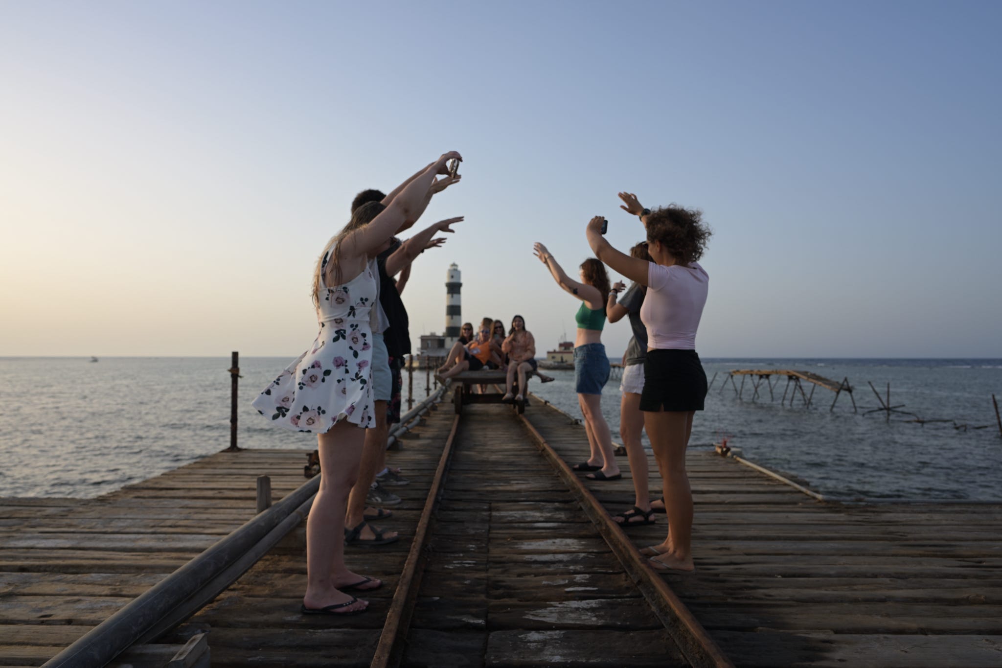 Friends on a reef jetty by a lighthouse at sunset, Red Sea, Egypt