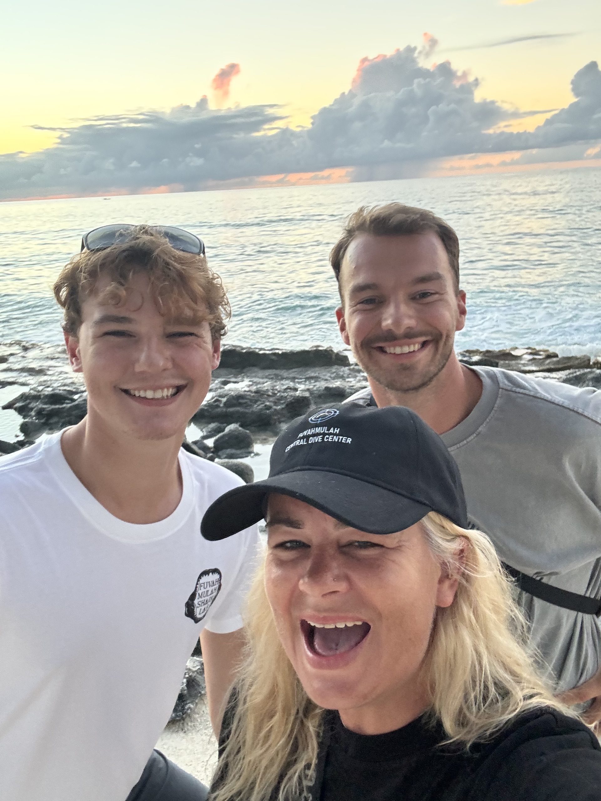 Three divers taking a selfie at sunset on the rocky shore, Fuvahmulah